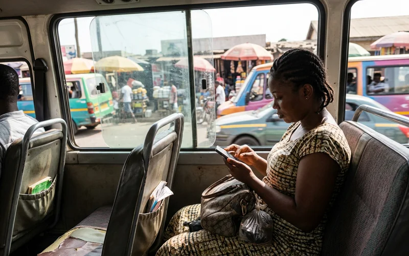 Customer on a bus in Accra tapping her phone, city traffic outside