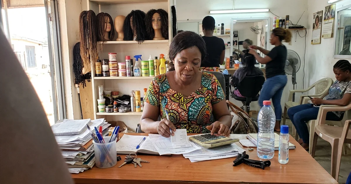 Salon owner in Kumasi reviewing invoices with a calculator at her reception desk